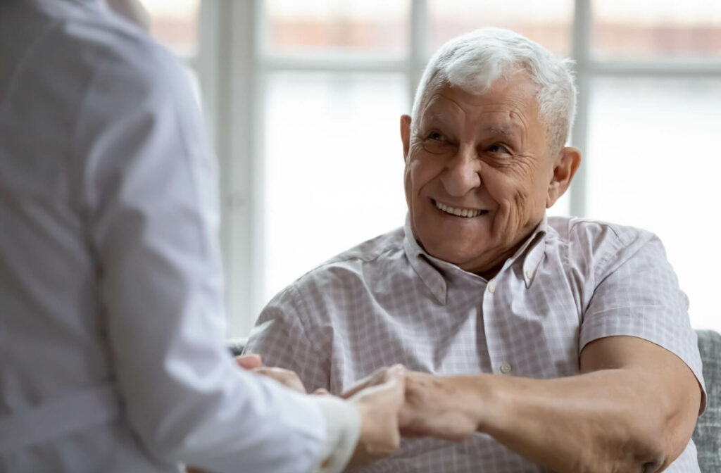 The back of a nurse holding hands with an older man why he smiles and looks at her