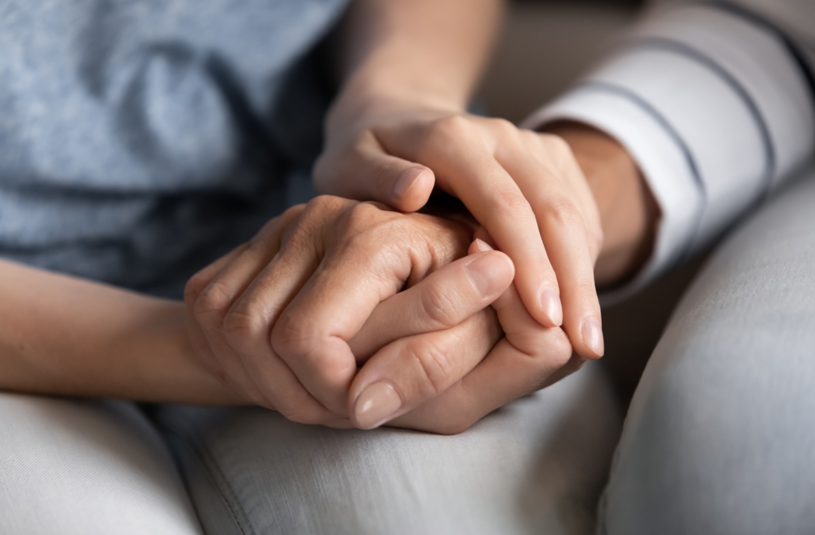 Close-up of an adult child cradling their senior parent's hand.