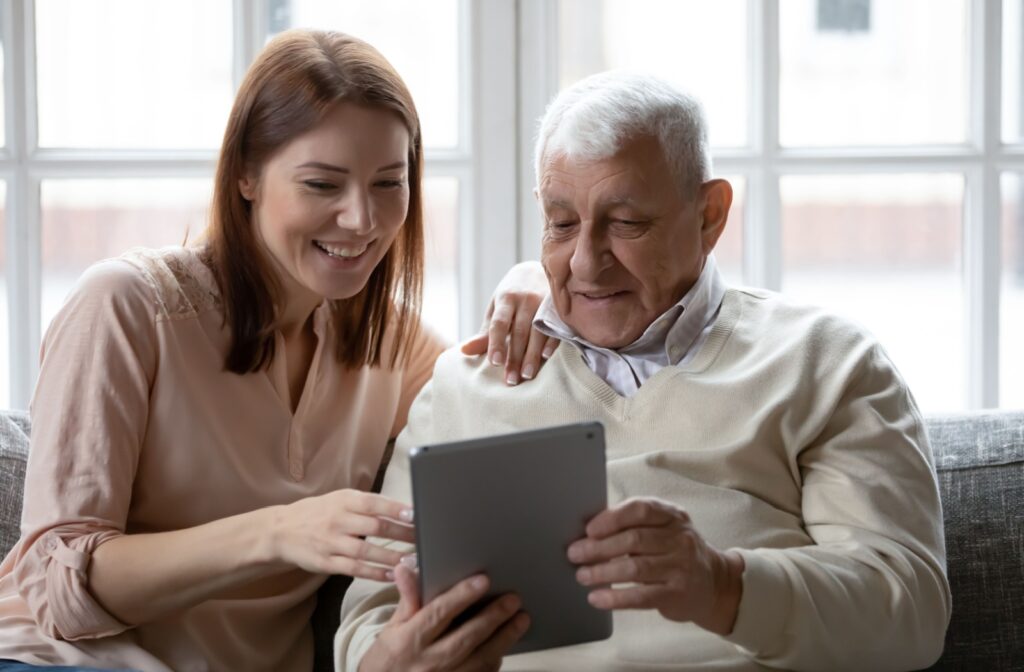 A woman sitting with her senior father and helping him use a tablet.