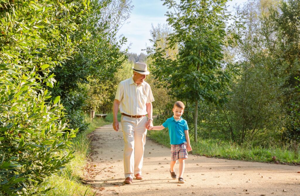 A grandfather walking with his grandson down a sunny nature path.