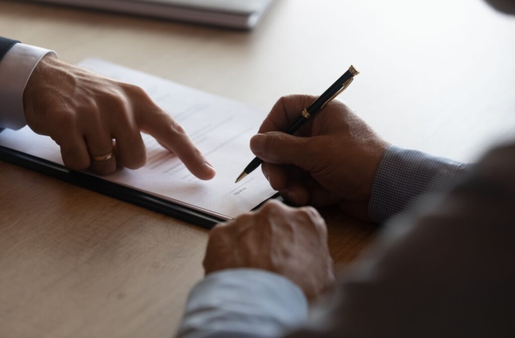 Close up of an older man signing a contract while the hand of a lawyer points to the signature line.