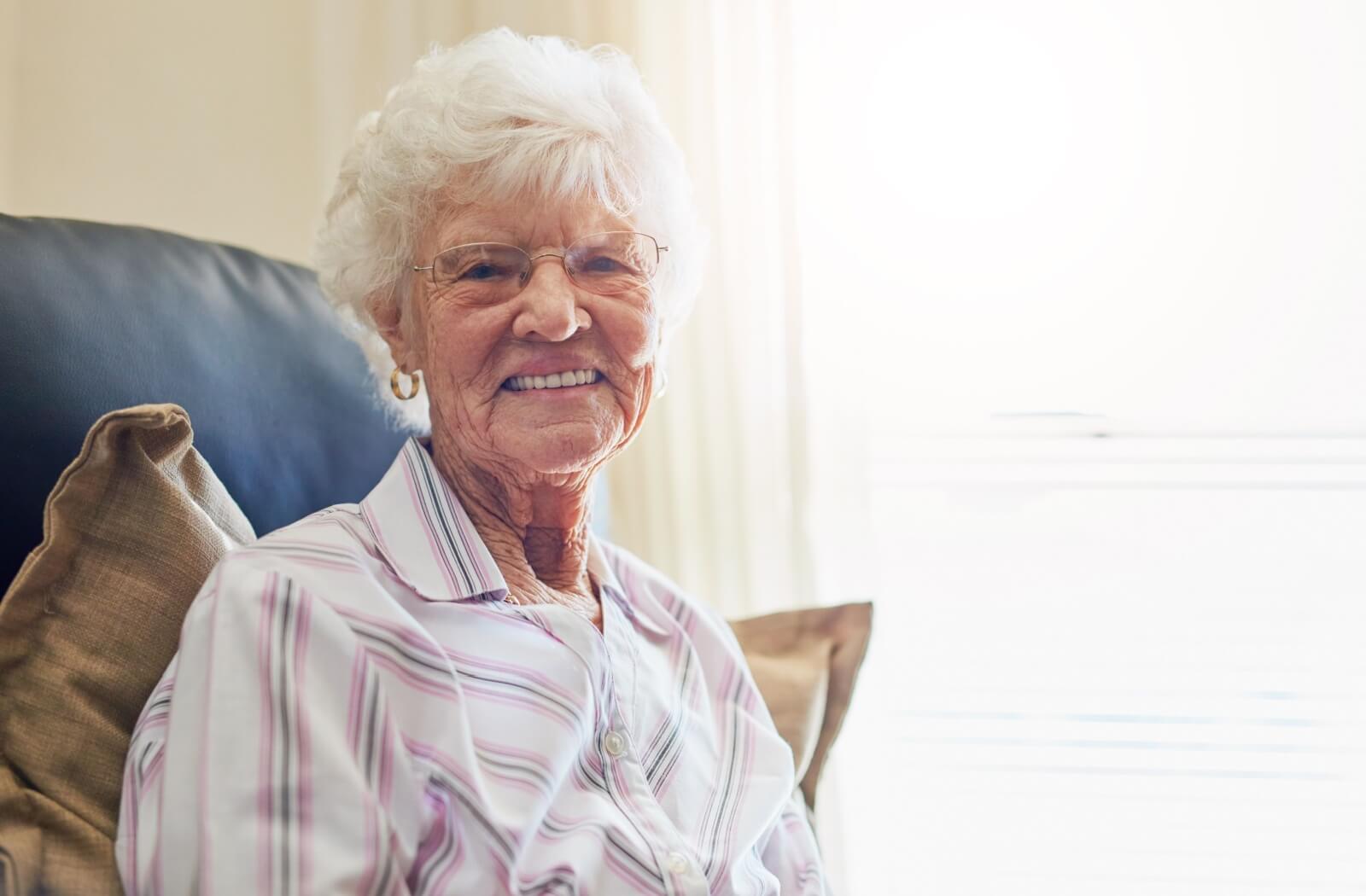 Smiling senior woman sitting comfortably in a well-lit room, radiating warmth and joy.