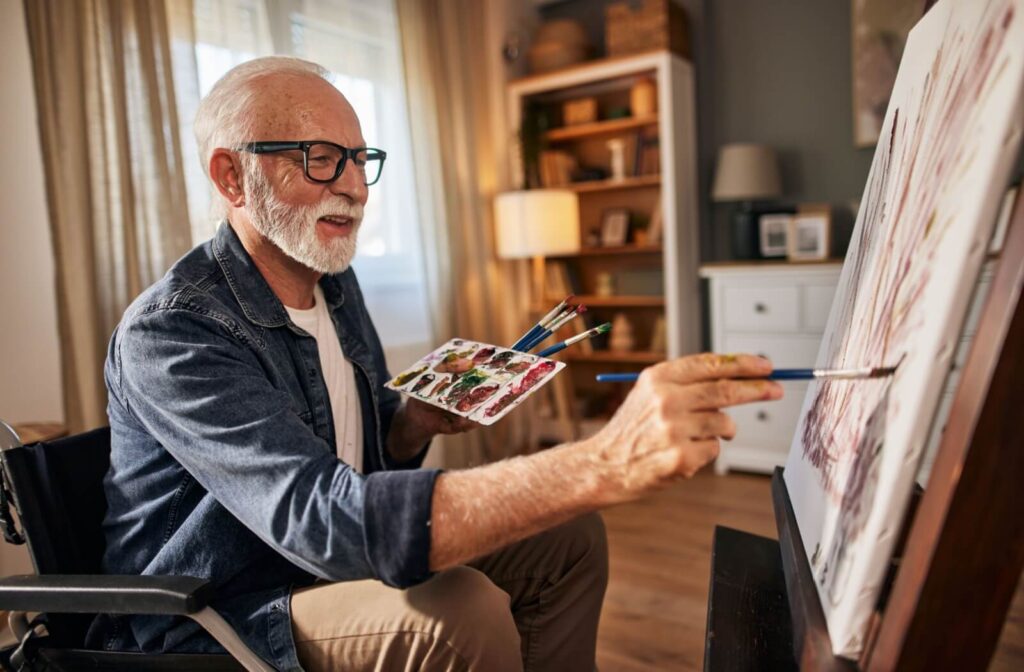 Senior man happily painting on a canvas in a cozy, well-lit room, showcasing creativity and engagement.