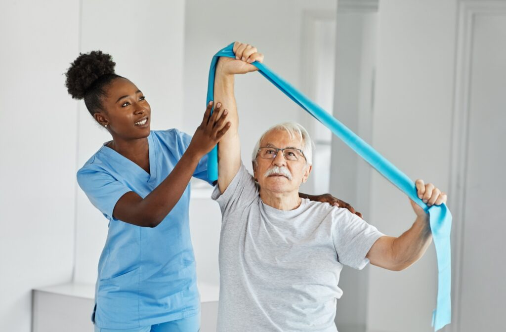 A nurse helping a senior man perform arm strengthening exercises with a resistance band.