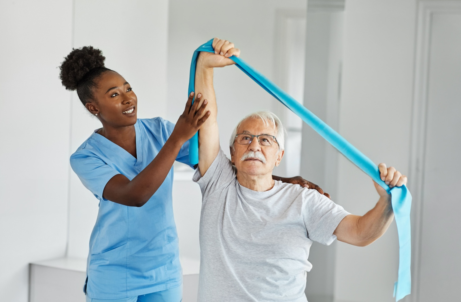 A nurse helping a senior man perform arm strengthening exercises with a resistance band.