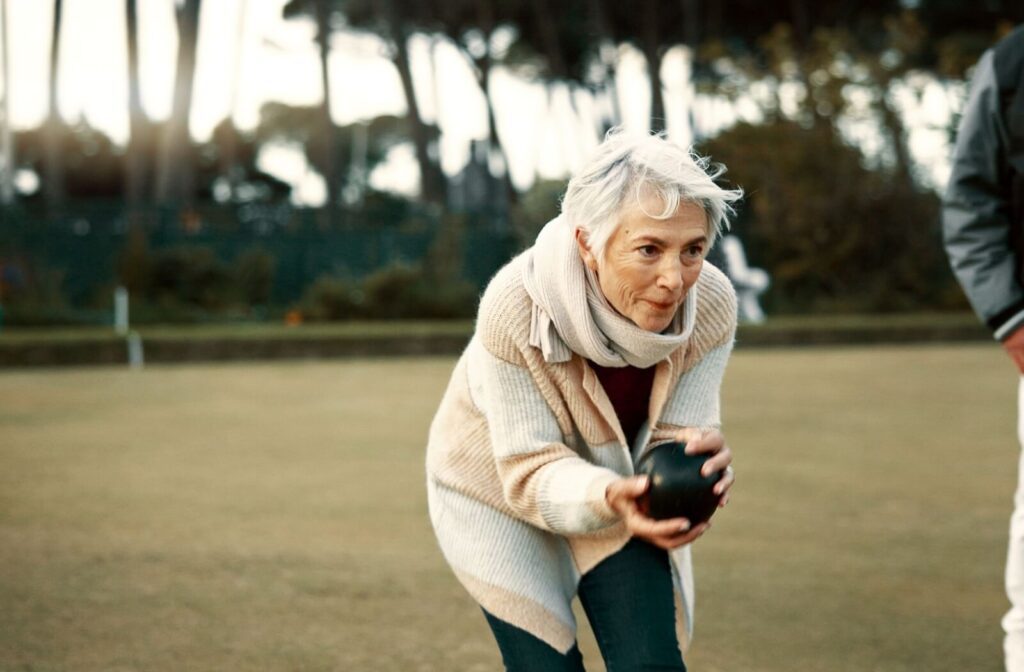 An older adult with dementia prepares to throw a bowling ball while lawn bowling.