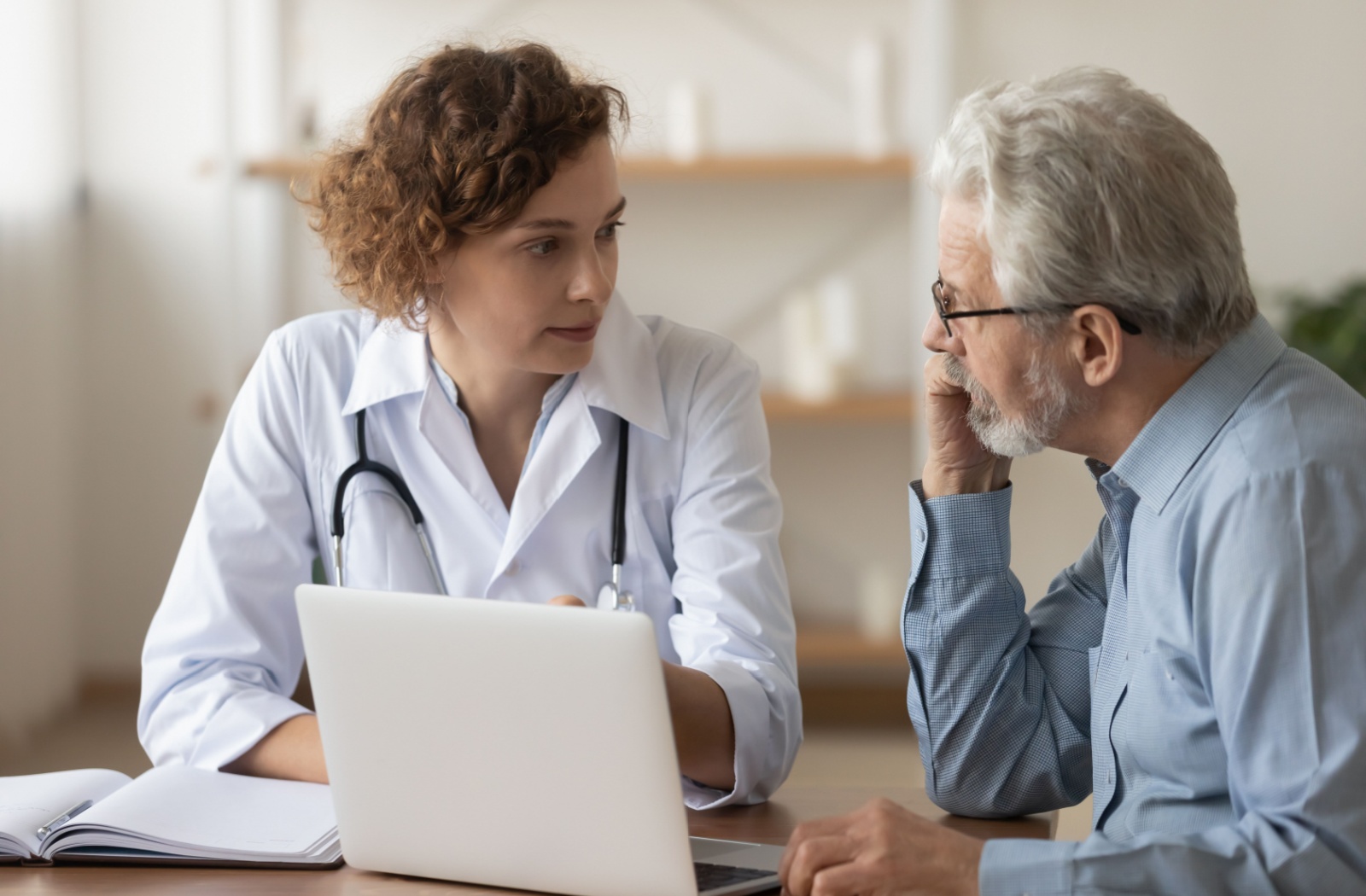 A healthcare working uses a laptop and notebook to show an older adult the results of their FAST score for dementia