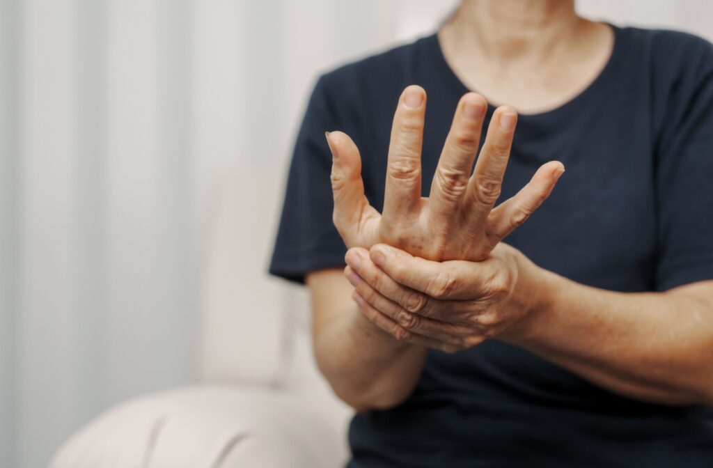 In a white room, a senior in a dark shirt holds their hand, massaging the muscle before performing a dementia assessment